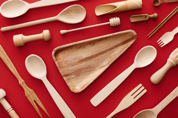 Vista superior del triángulo vacío plato de madera sobre fondo rojo con utensilios de cocina — Stock Photo