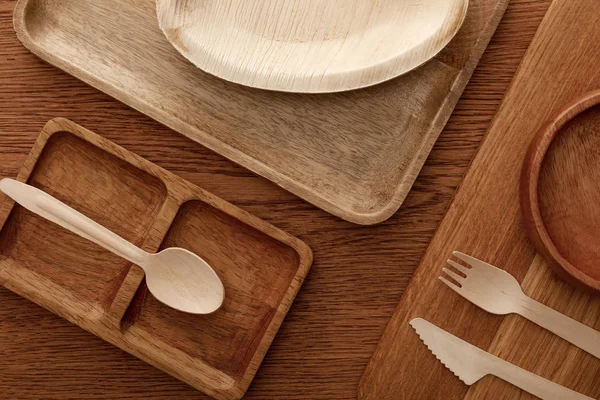 Vue de dessus de plat en bois et planche à découper avec assiettes et couverts sur fond brun — Photo de stock