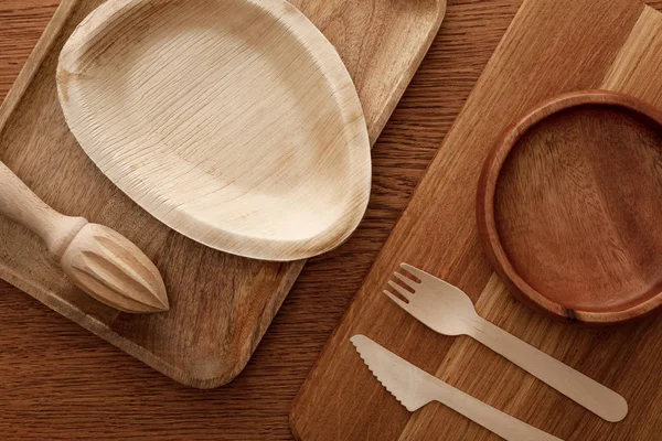 Top view of wooden dish and cutting board with plates, cutlery and hand juicer on brown background — Stock Photo