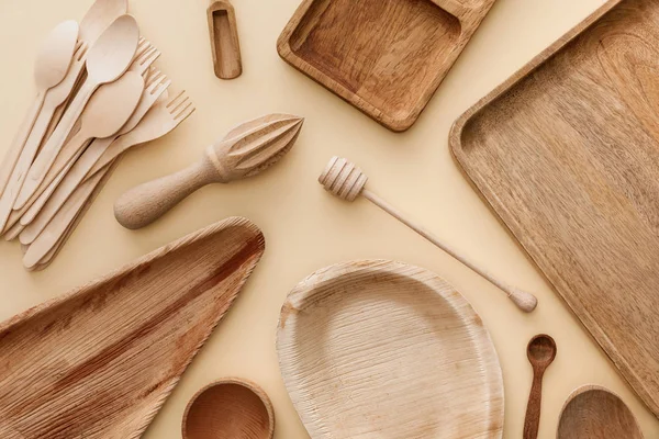 Vue de dessus des assiettes en bois, plats, fourchettes, cuillères et presse-agrumes à main sur fond beige — Photo de stock