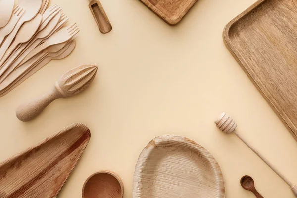 Вид зверху на дерев'яні тарілки, посуд, виделки, ложки та ручний соковижималка на бежевому фоні з місцем для тексту — стокове фото