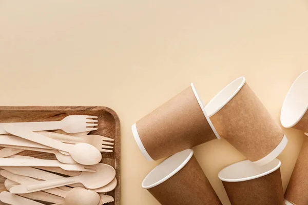 Top view of rectangular wooden dish with forks and spoons near paper cups on beige background — Stock Photo