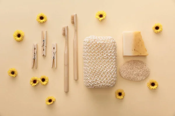 Vista superior de pinzas de madera, cepillos de dientes, esponja de baño, jabón natural y esponja sobre fondo beige con flores - foto de stock