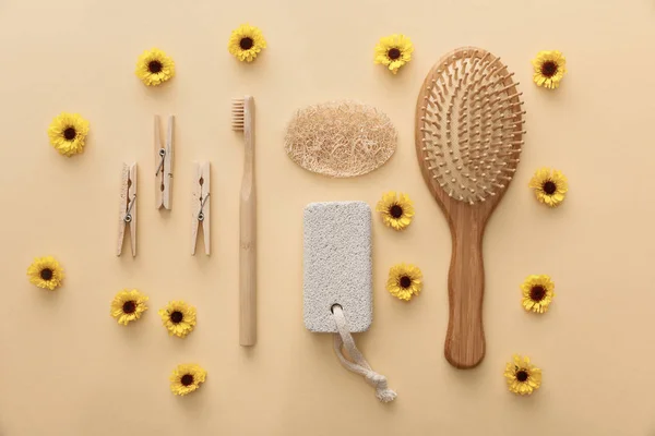 Vista superior de pinzas de tela de madera, cepillo de dientes, cepillo de pelo, piedra pómez y esponja sobre fondo beige con flores - foto de stock