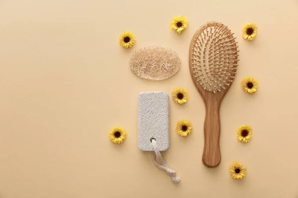 Draufsicht auf hölzerne Haarbürste, Bimsstein und Luffa auf beigem Hintergrund mit Blumen — Stockfoto