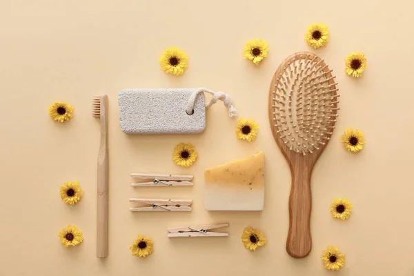 Vista superior de pinzas de madera, cepillo de dientes, cepillo de pelo, piedra pómez y jabón sobre fondo beige con flores - foto de stock