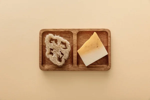 Top view of brown wooden soapdish with loofah and piece of soap on beige background — Stock Photo