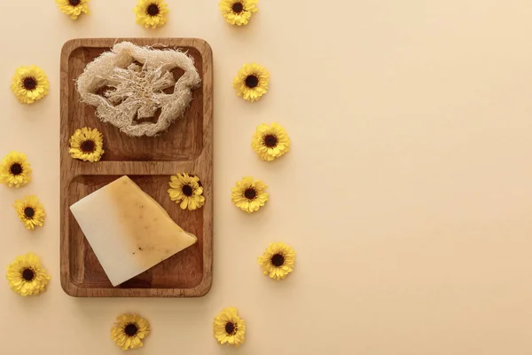 Vista superior de jabón marrón de madera con esponja y jabón sobre fondo beige con flores - foto de stock