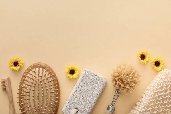 Vista dall'alto di spazzolino da denti, spazzola per capelli, spazzola per il corpo, spugna da bagno e pietra pomice su sfondo beige con fiori — Foto stock