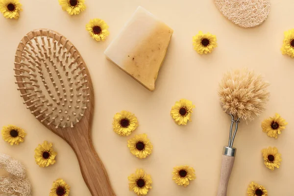 Draufsicht auf Haarbürste, Körperbürste, Luffa und Seife auf beigem Hintergrund mit Blumen — Stockfoto