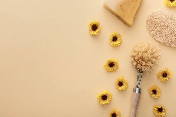 Top view of body brush, loofah and piece of soap on beige background with flowers and copy space — Stock Photo