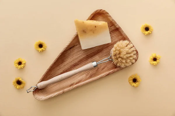 Vista superior de triángulo plato de madera con jabón y cepillo de cuerpo sobre fondo beige con flores - foto de stock