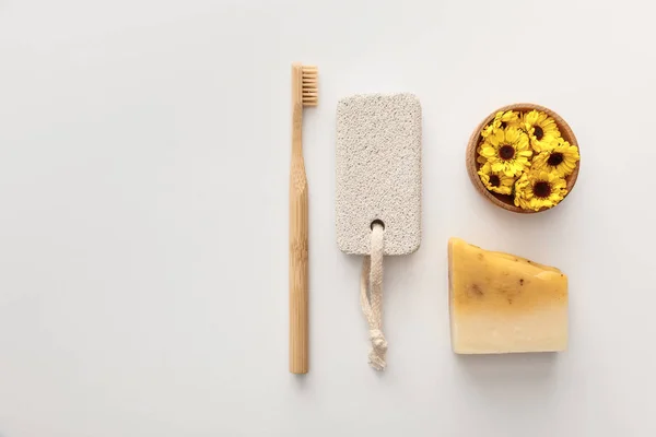 Pose plate avec brosse à dents, morceau de savon, pierre ponce et tasse avec des fleurs sur fond blanc — Photo de stock