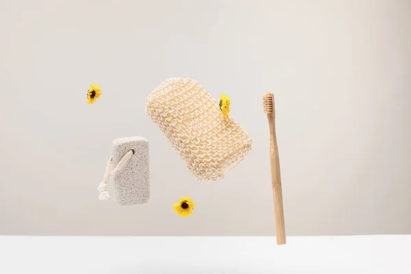 Toothbrush, pumice stone, bath sponge and flowers isolated on gray — Stock Photo