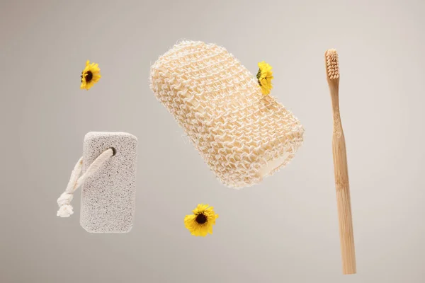 Toothbrush, pumice stone, bath sponge and yellow flowers isolated on gray — Stock Photo