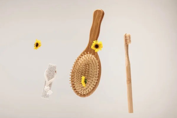 Brosse à dents, pierre ponce, brosse à cheveux et fleurs jaunes isolées sur gris — Photo de stock