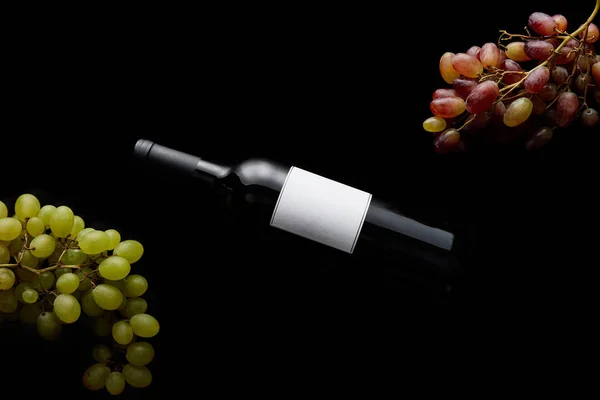 Top view of wine bottle with blank white label near ripe grape isolated on black — Stock Photo