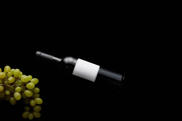 Top view of wine bottle with blank white label near ripe grape isolated on black — Stock Photo