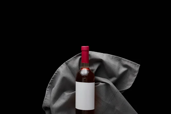 Vista superior de la botella de vino rosa con etiqueta blanca en blanco en servilleta gris aislada en negro - foto de stock