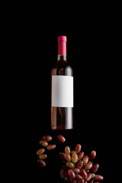 Top view of bottle with rose wine and blank white label near grape isolated on black — Stock Photo