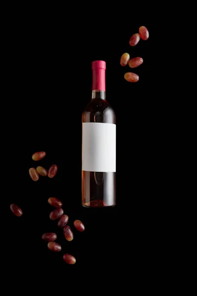 Top view of rose wine bottle with blank white label near ripe grape isolated on black — Stock Photo