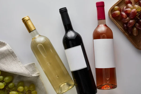 Top view of bottles with white, red and rose wine near grape on white background — Stock Photo