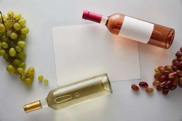 Top view of bottles with white and rose wine near grape and blank card on white background — Stock Photo