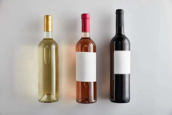 Plat posé avec des bouteilles de vin blanc, rose et rouge sur fond blanc — Photo de stock