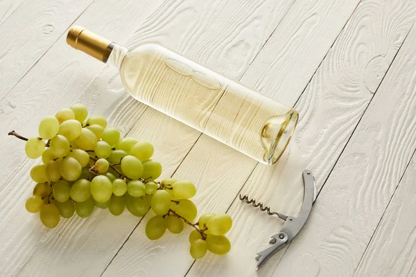 Botella con vino blanco cerca de la uva y sacacorchos en la superficie de madera blanca - foto de stock