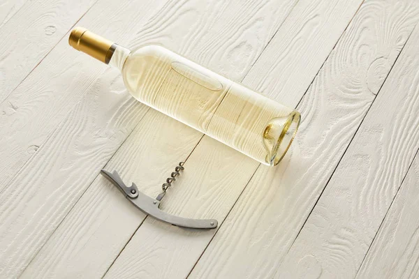 Bottle with white wine near corkscrew on white wooden surface — Stock Photo