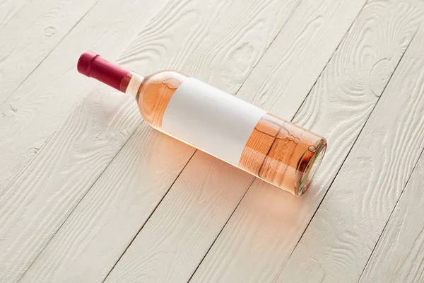 Garrafa com vinho rosa e etiqueta em branco na superfície de madeira branca — Fotografia de Stock