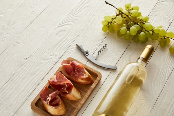 Flasche mit Weißwein in Traubennähe, Schinken auf Baguette und Korkenzieher auf weißer Holzoberfläche — Stockfoto