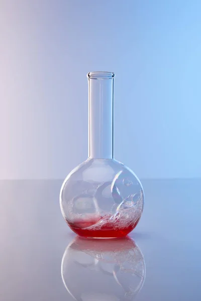 Frasco de vidrio con colorido líquido rojo sobre fondo azul - foto de stock