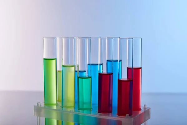 Glas-Reagenzgläser mit bunter Flüssigkeit auf blauem Hintergrund — Stockfoto