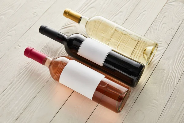Garrafas com vinho tinto, branco e rosa na superfície de madeira branca — Fotografia de Stock