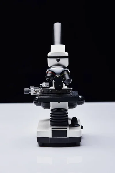 Modern microscope on white table isolated on black — Stock Photo