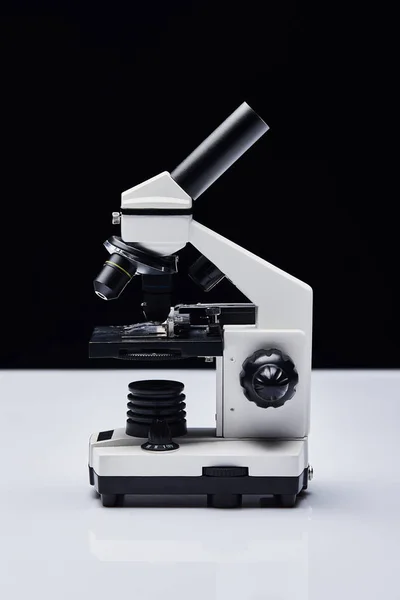 Modern microscope on white table isolated on black — Stock Photo