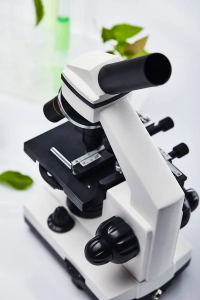 Foco seletivo do microscópio perto de tubos de ensaio de vidro com líquido colorido e folhas — Fotografia de Stock