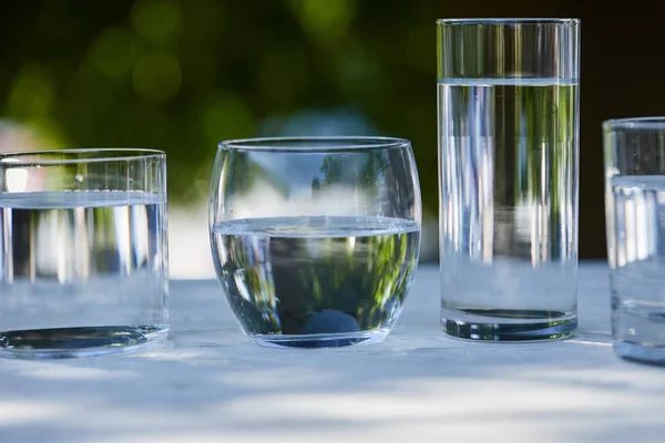 Eau douce claire dans des verres transparents à la lumière du soleil sur une table en bois — Photo de stock