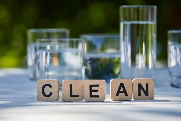 Saubere Schriftzüge auf Blöcken in der Nähe von Süßwasser in transparenten Gläsern im Sonnenlicht auf Holztisch — Stockfoto