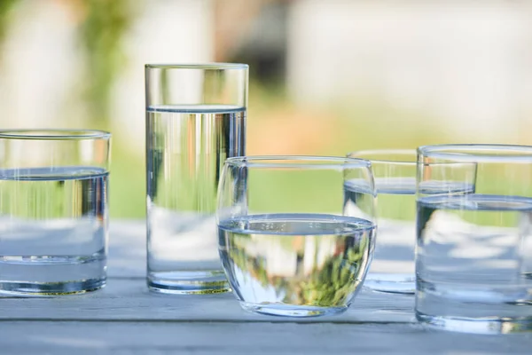 Eau douce claire dans des verres transparents à la lumière du soleil sur une table en bois — Photo de stock