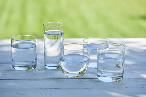 Clear fresh water in transparent glasses in sunlight on wooden table — Stock Photo