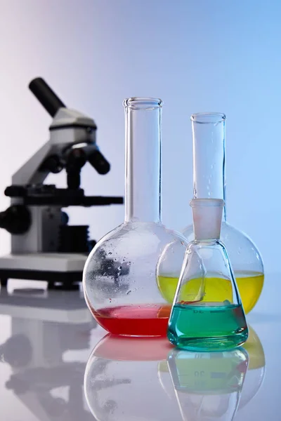 Foco seletivo de frascos de vidro com líquido colorido próximo ao microscópio — Fotografia de Stock