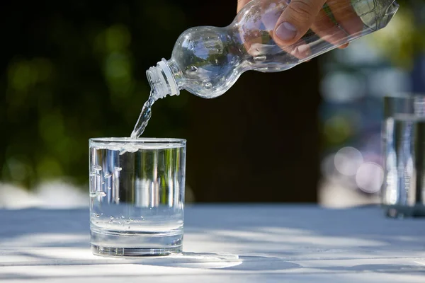 Vista cortada do homem derramando água limpa de garrafa de plástico em vidro — Fotografia de Stock