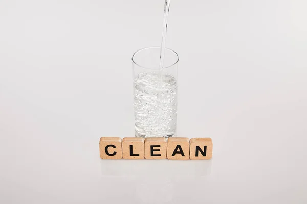 Acqua dolce limpida versando in vetro vicino a cubi con scritte pulite su fondo grigio — Foto stock