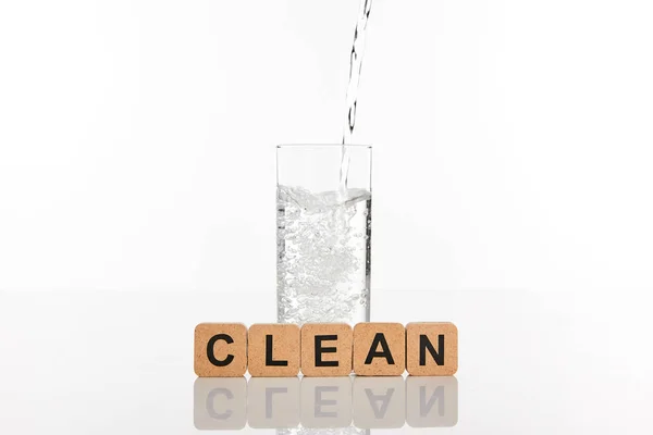 Acqua dolce limpida versando in vetro vicino a cubi con scritte pulite isolate su bianco — Foto stock