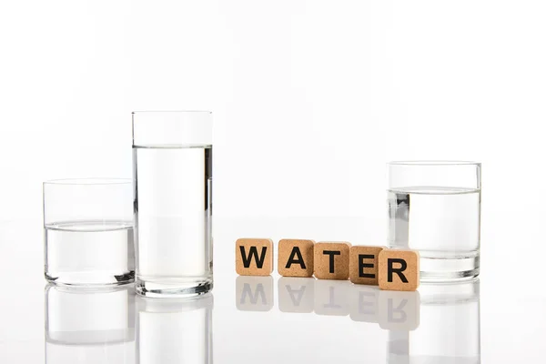 Limpida acqua dolce in bicchieri vicino a cubi con scritta acqua isolata su bianco — Foto stock