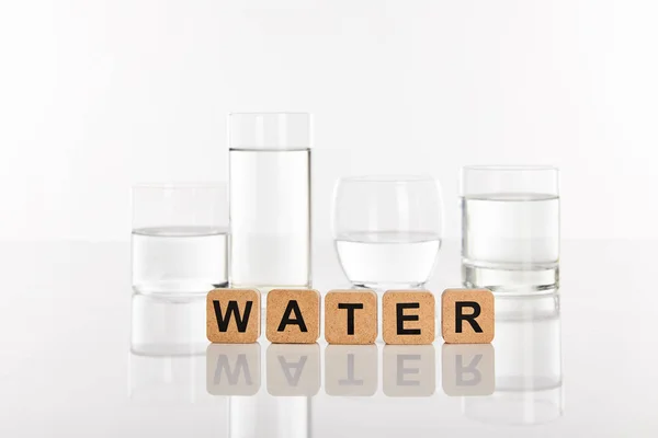 Clear fresh water in glasses near cubes with water lettering isolated on white — Stock Photo