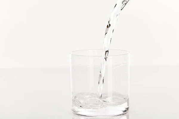 Прозора прісна вода, що ллється в склянку ізольовано на білому — стокове фото