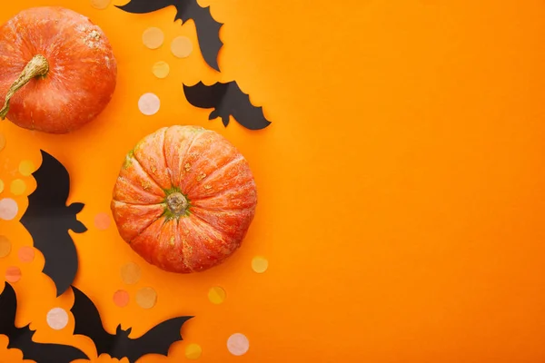 Vue de dessus de citrouille, chauves-souris et confettis sur fond orange, décoration d'Halloween — Photo de stock